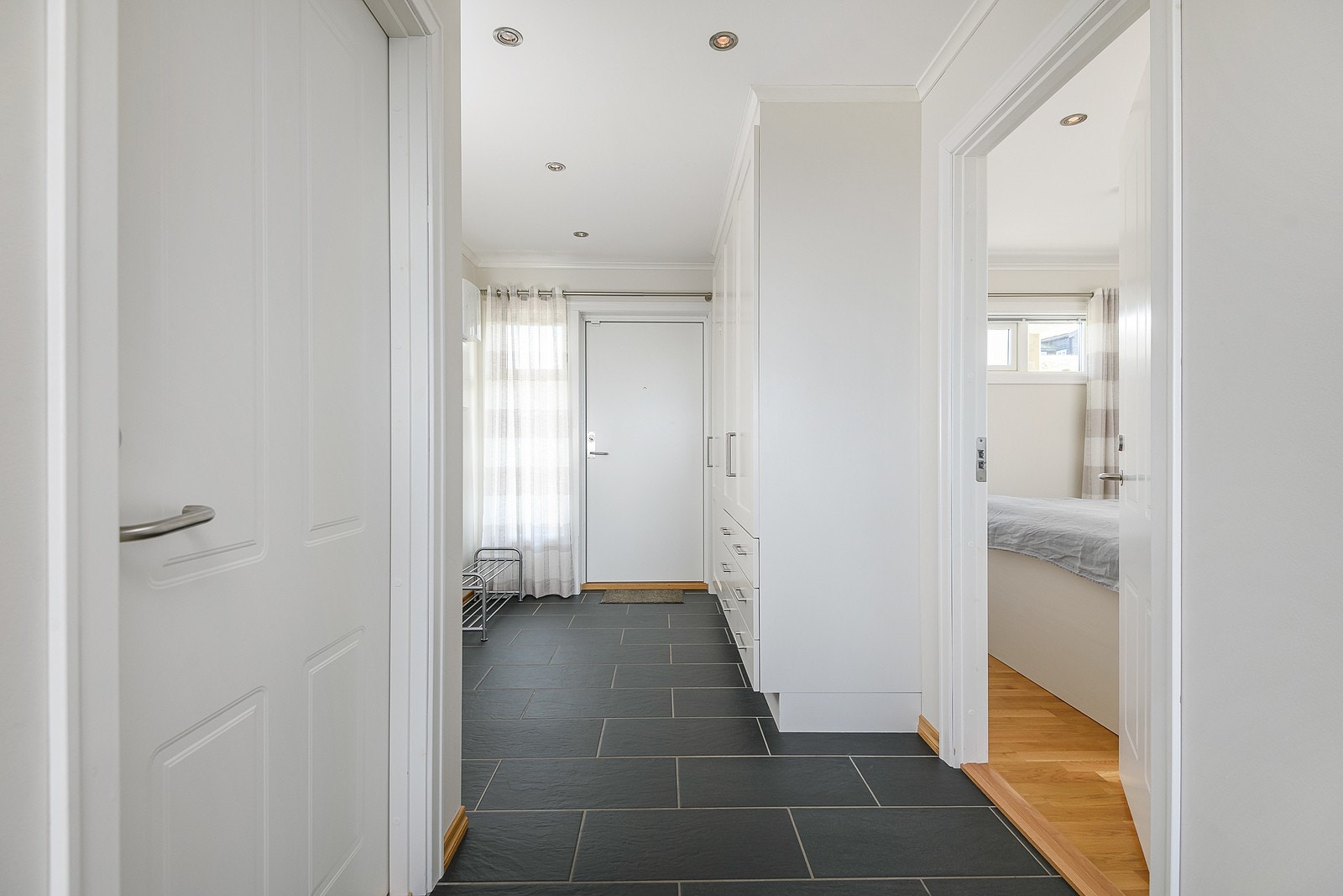 Entréen er romslig og pen, innredet med mørke gulvfliser med gulvvarme, downlights og lyse veggflater. Garderobeskap (inkl. tørkeskap) med profilerte, lyse fronter. Galleribilde