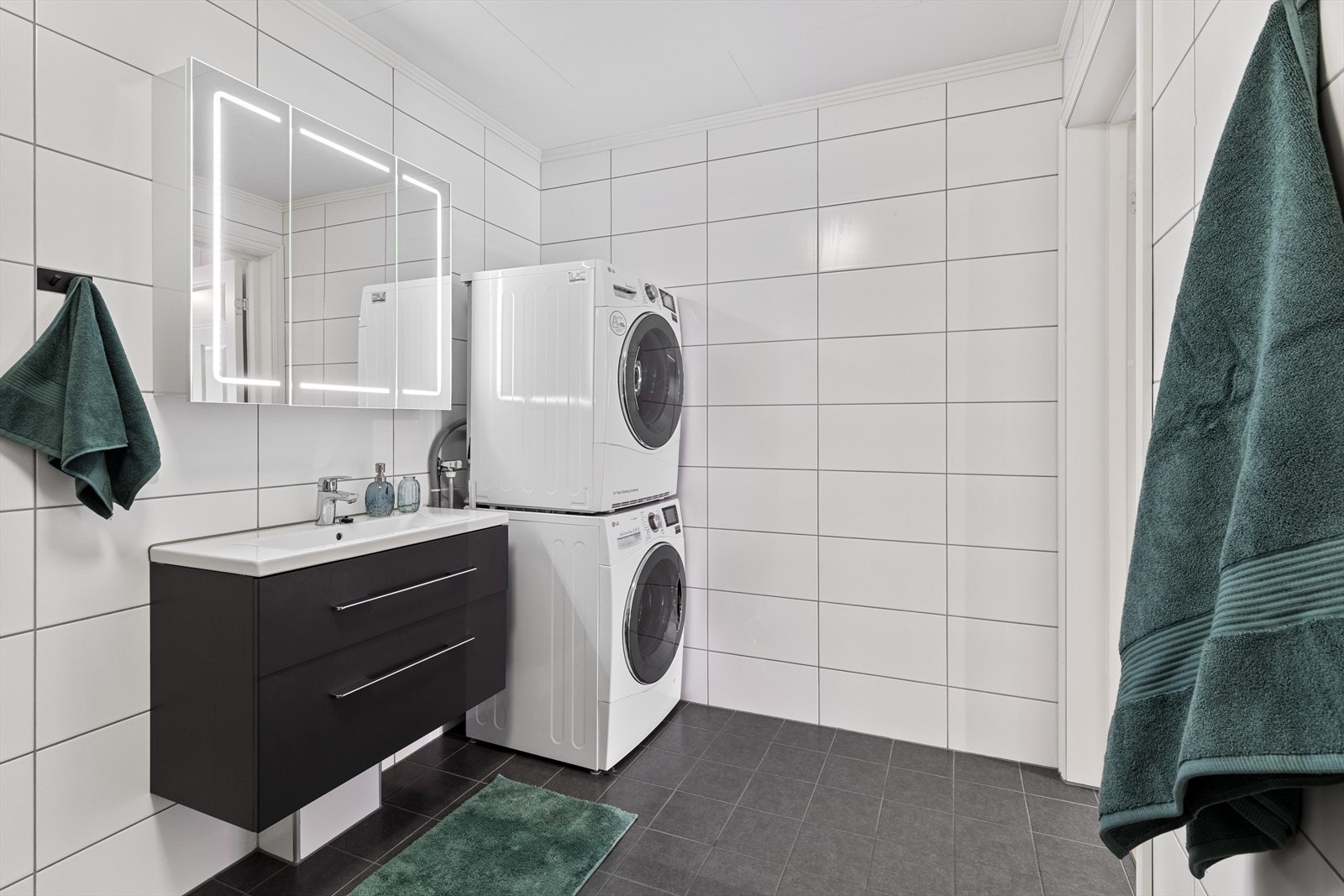 Boligen har et pent bad med flislagte flater og gulvvarme. Innbydende baderomsinnredning med mørke skuffefronter og heldekkende servant, samt et flott speil med integrert belysning. Galleribilde