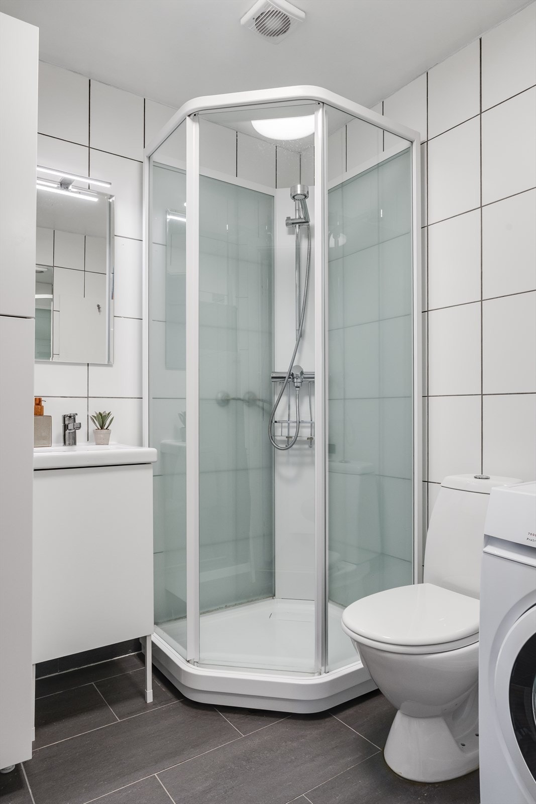 Badet er innredet/utstyrt med dusjkabinett, servant med skap, speil med belysning, toalett samt opplegg for vaskemaskin. Galleribilde