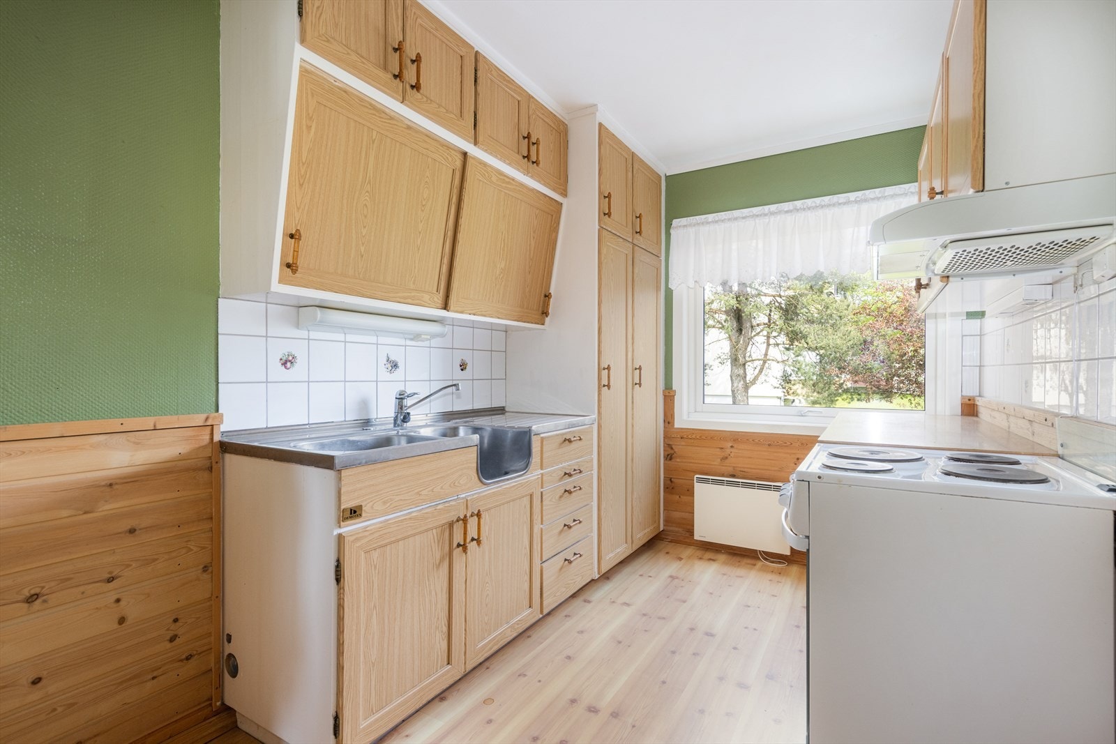 Kjøkkenet har en eldre innredning med profilerte fronter, laminat benkeplate og benkebeslag, samt flis over kjøkkenbenk. Galleribilde