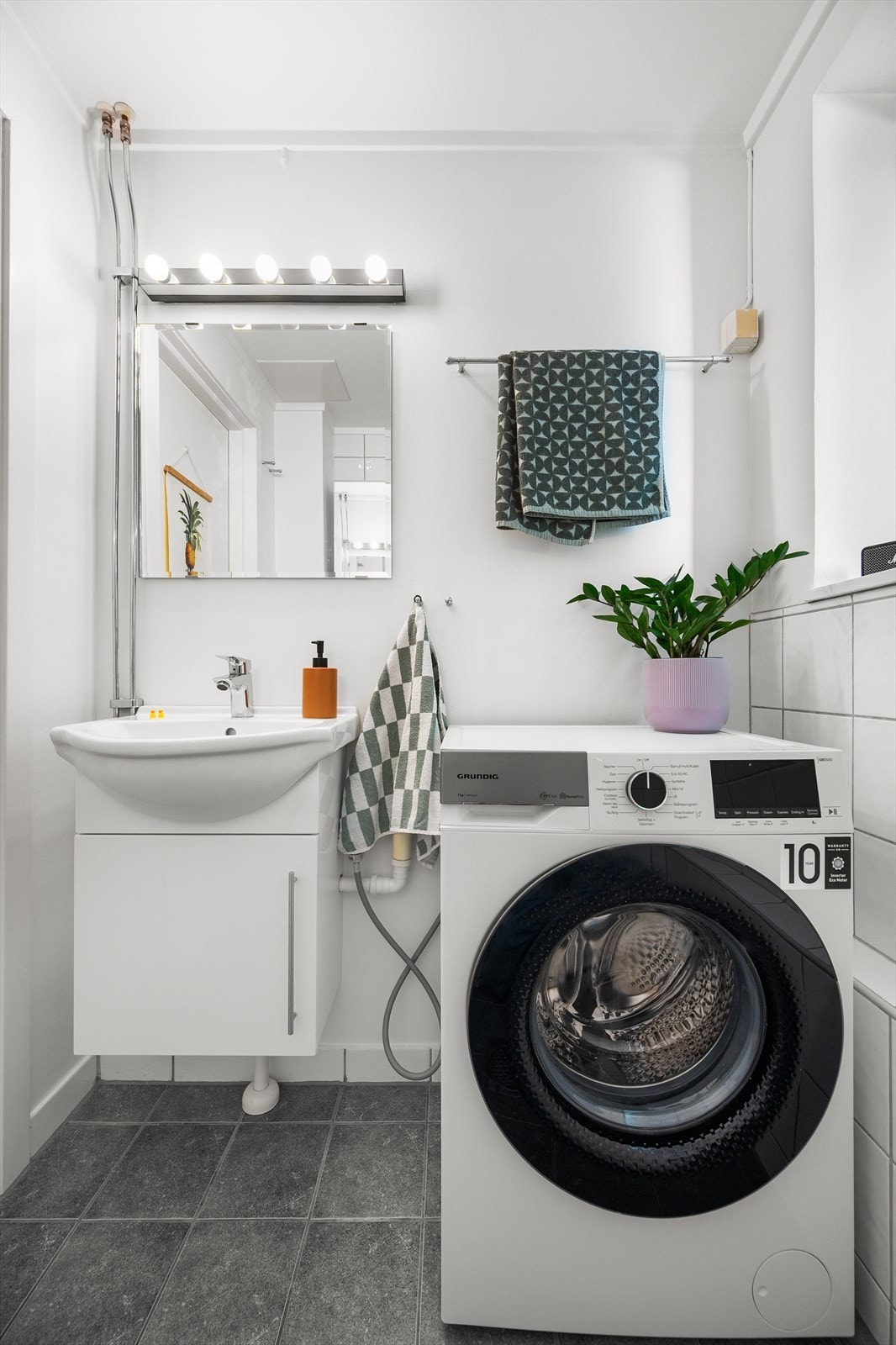 Badet er innredet med gulvmontert toalett, dusjhjørne med forheng og baderomsinnredning med servant, blandebatteri, skap og vegghengt speil. Galleribilde