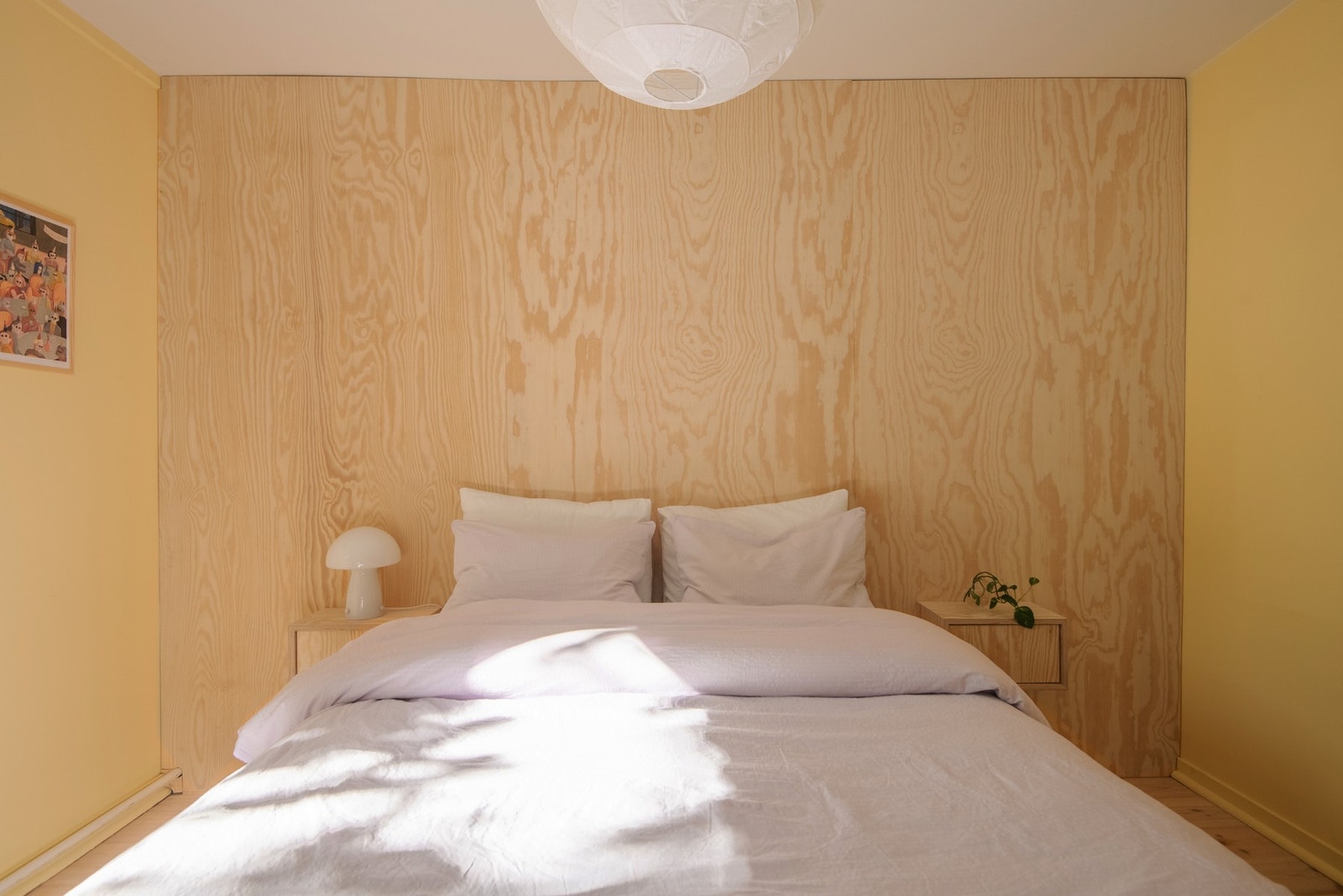 Veggene på soverommet ble malt i 2024 i en varm gulfarge som harmonerer vakkert med en kontrastvegg i kryssfiner med vegghengte nattbord, spesiallaget av møbelsnekker. Galleribilde