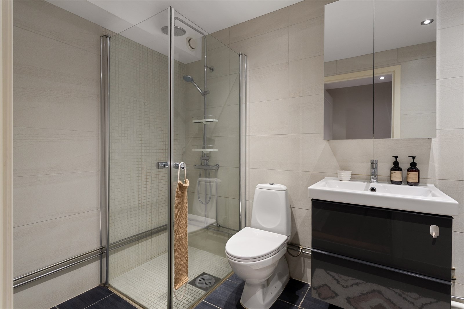 Baderommet er innredet med klosett, servant nedfelt i innredning, speilskap og dusjhjørne med svingbare glassdører. Galleribilde