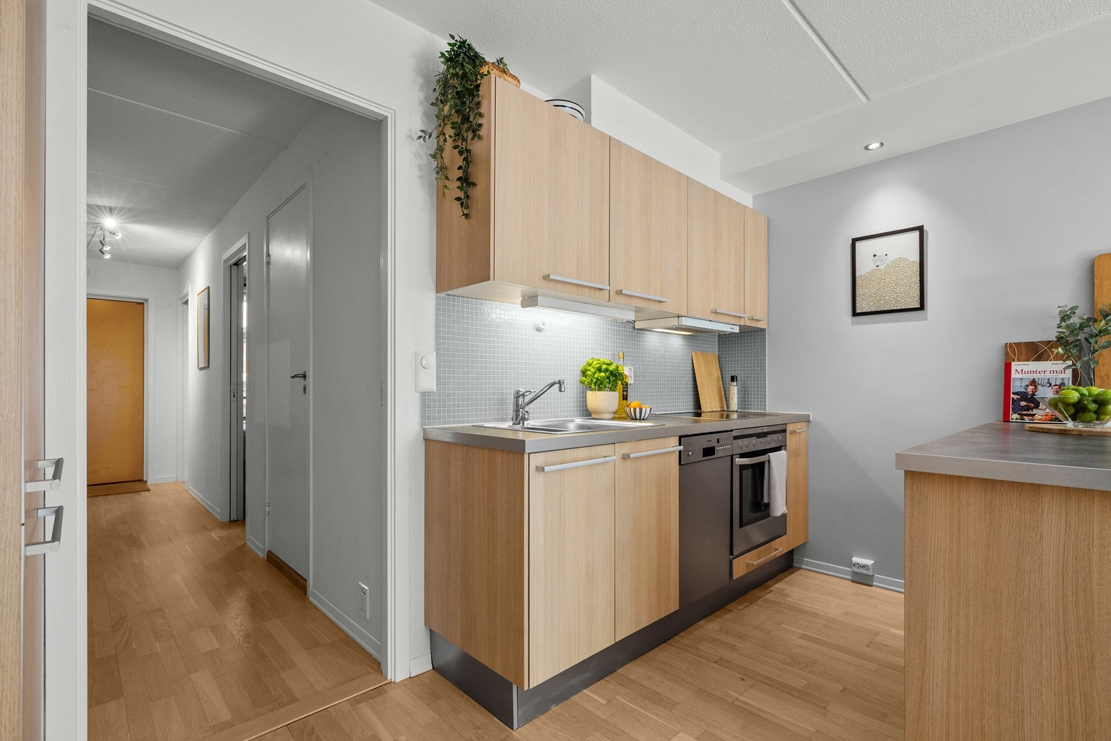 Lys kjøkkeninnredning med slette fronter, laminat benkeplate, toppmontert kum, ett- greps blandebatteri. Galleribilde