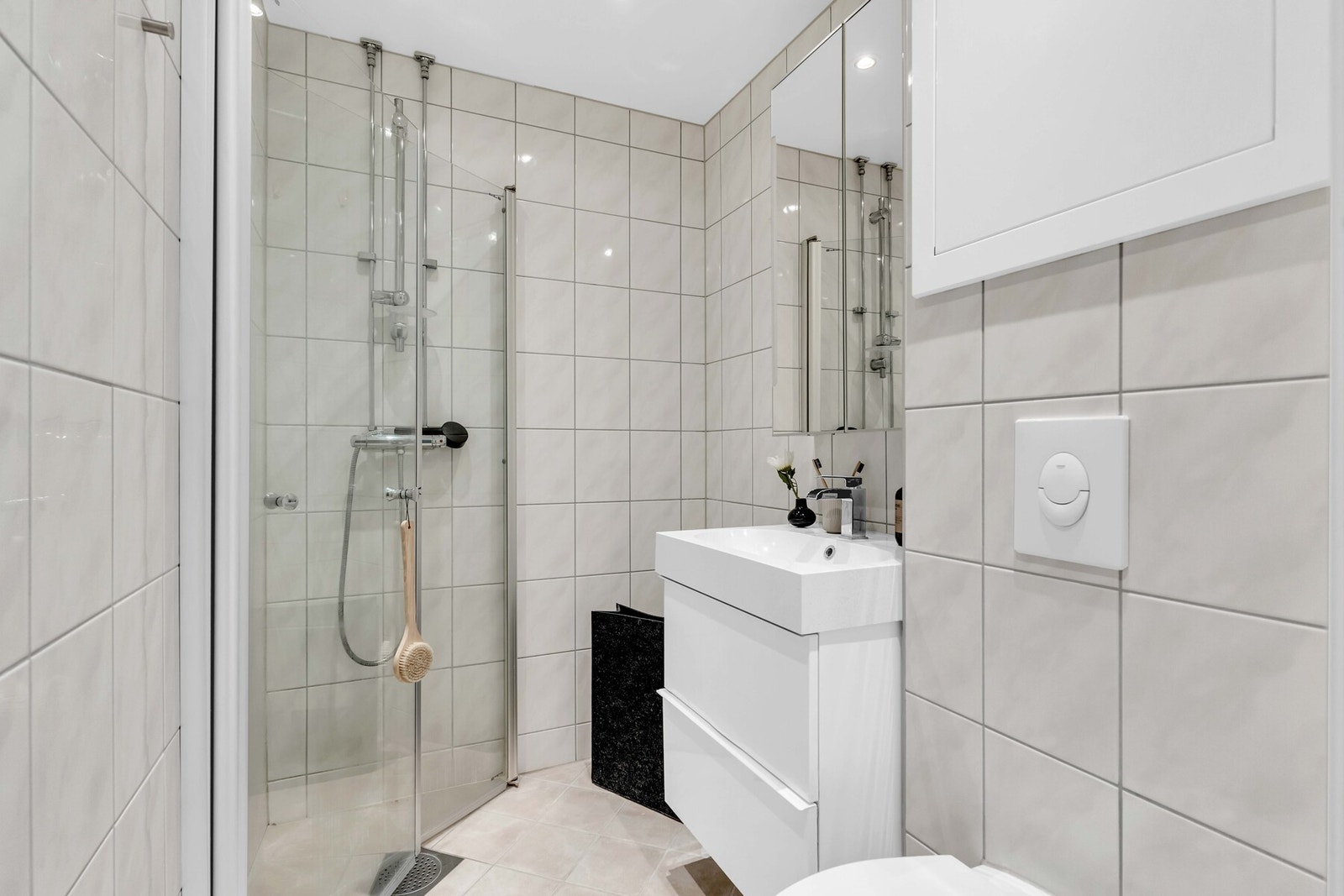 Et stilrent flislagt baderom fra 2016 med vegghengt servant, speilskap, toalett og dusj med innfellbare dører. Galleribilde