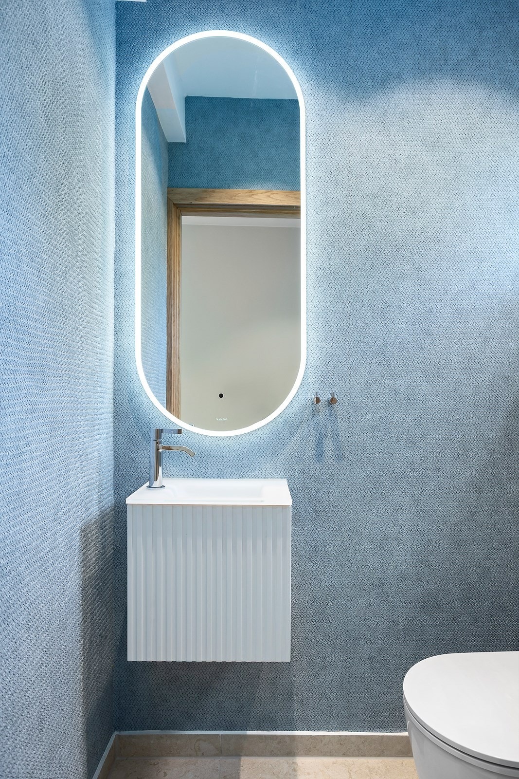 Toalettrom med flislagt gulv og varmekabler, tapet på veggene. Rommet er utstyrt med et stilrent 40 cm bredt servantskap med profilert front og frostet glass servant med ettgreps blandebatteri i rustfritt stål fra Tapwell. Galleribilde