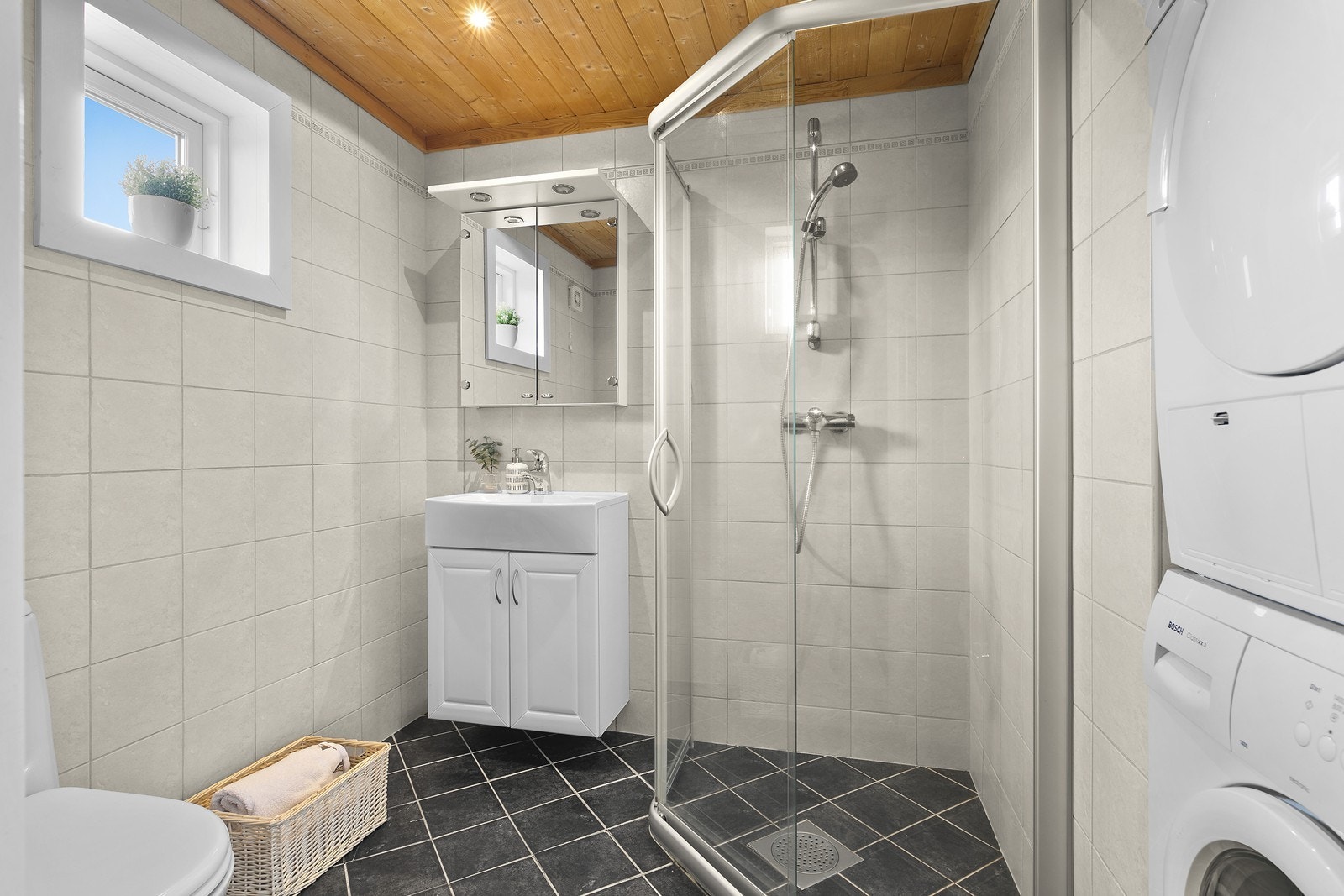 Badet har flislagt gulv med varmekabler. Rommet inneholder dusjnisje, servant med underskap og speil, WC og vaskemaskin. Galleribilde