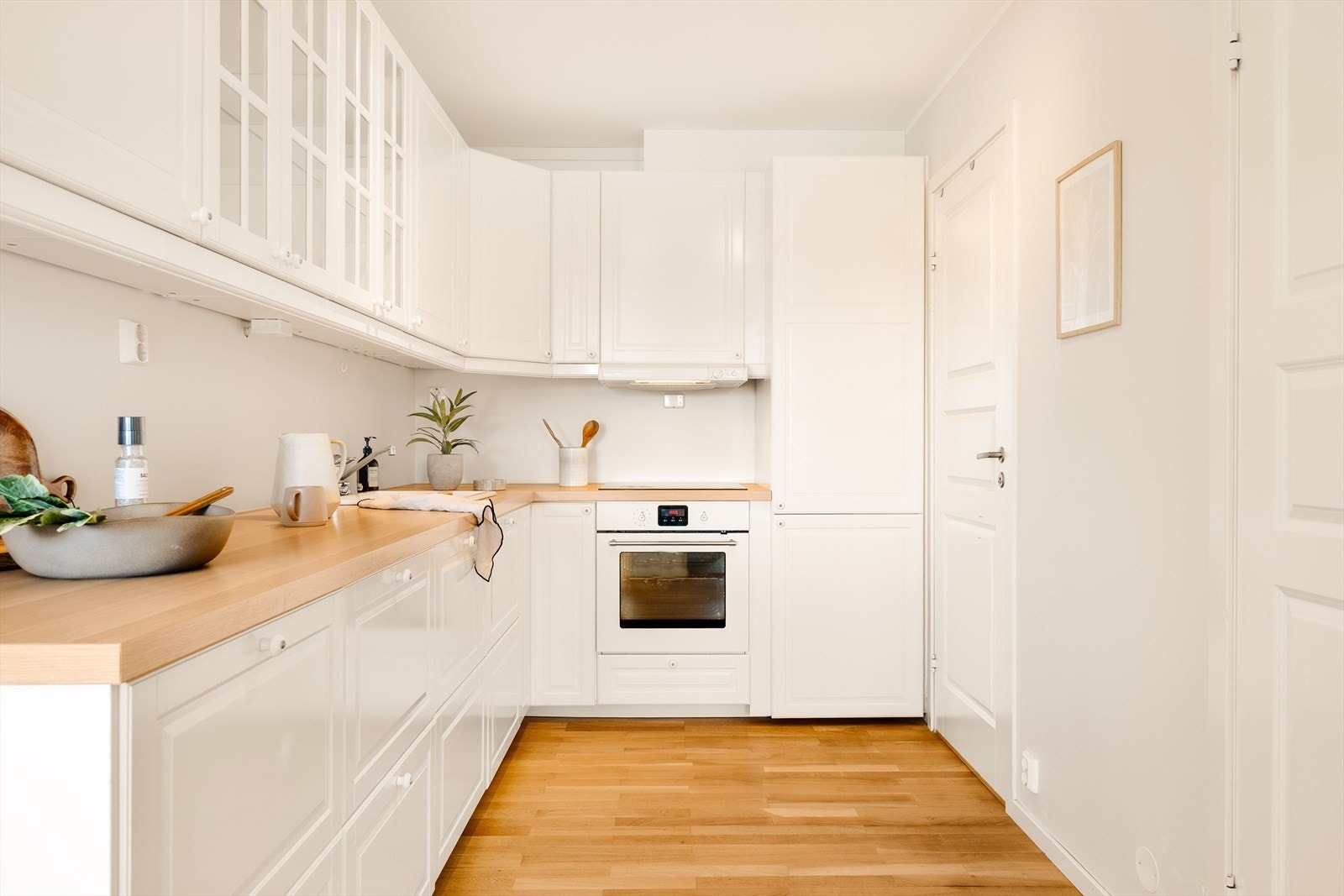 Kjøkkenet har en stilren innredning med profilerte fronter, to overskap med glassfronter, laminat benkeplate, over benkeplaten er det benyttet malte flater, oppvaskkum og ventilator Galleribilde