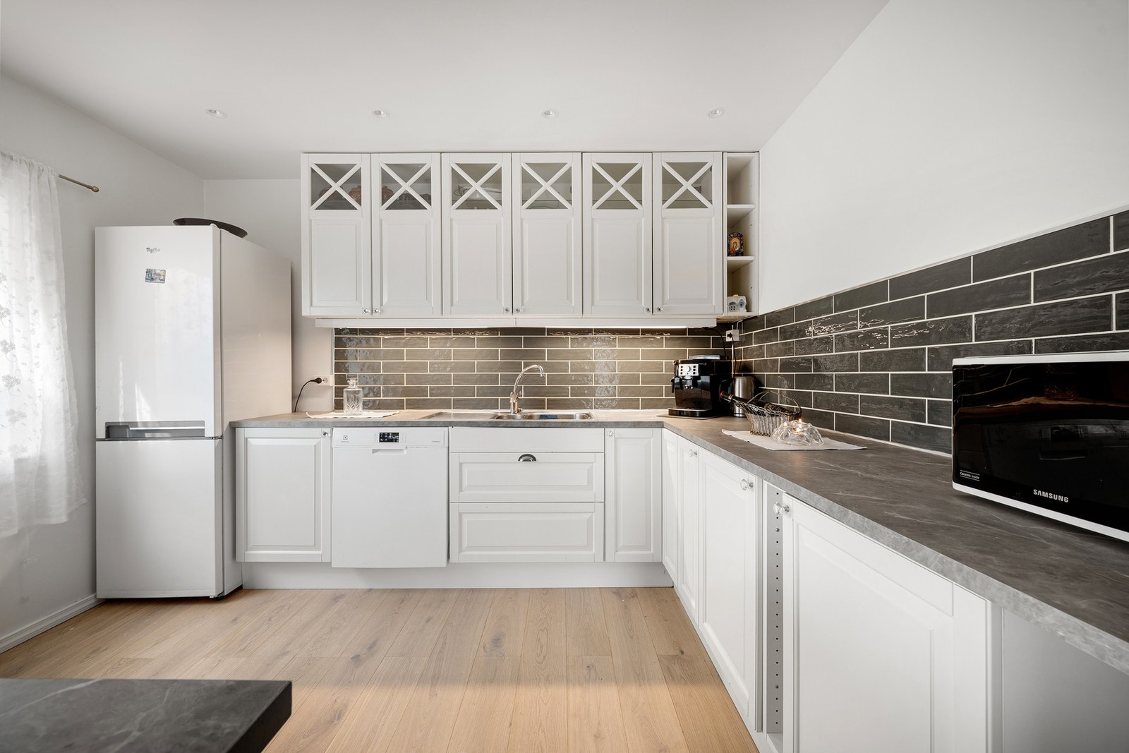 Pen innredning med hvite profilerte fronter og takhøye overskap med glassfelter Galleribilde