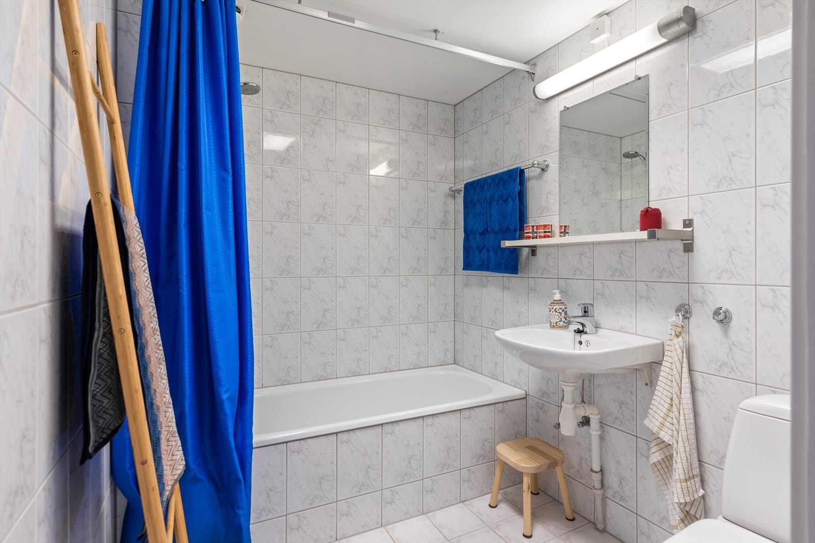 Lyst og helfliset baderom med fliser på vegger og gulv. Videre er badet innredet med baderomsinnredning, badekar og gulvmontert toalett. Galleribilde