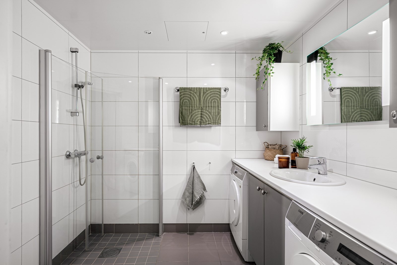 Badet fremstår lyst, ryddig og moderne - med rene linjer og smarte løsninger som kombinerer estetikk og funksjon. Hvite, store fliser på veggene gir rommet et tidløst uttrykk, mens innredning i dempet gråfarge tilfører kontrast og eleganse. Galleribilde