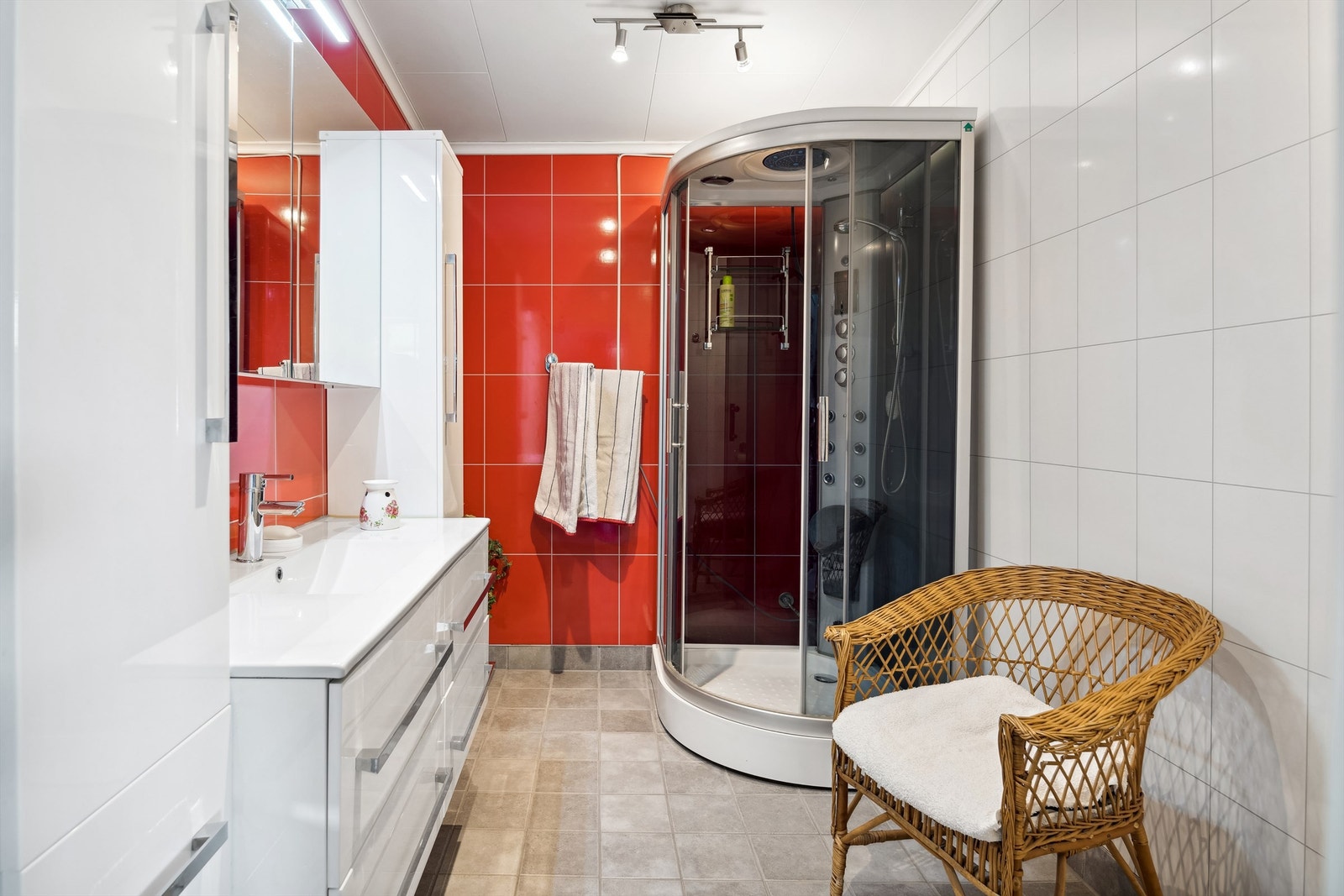 Badet har fliser på gulv med elektrisk gulvvarme og baderomsplater på vegger. Badet er innredet med toalett, servant i innredning og dusjkabinett Galleribilde