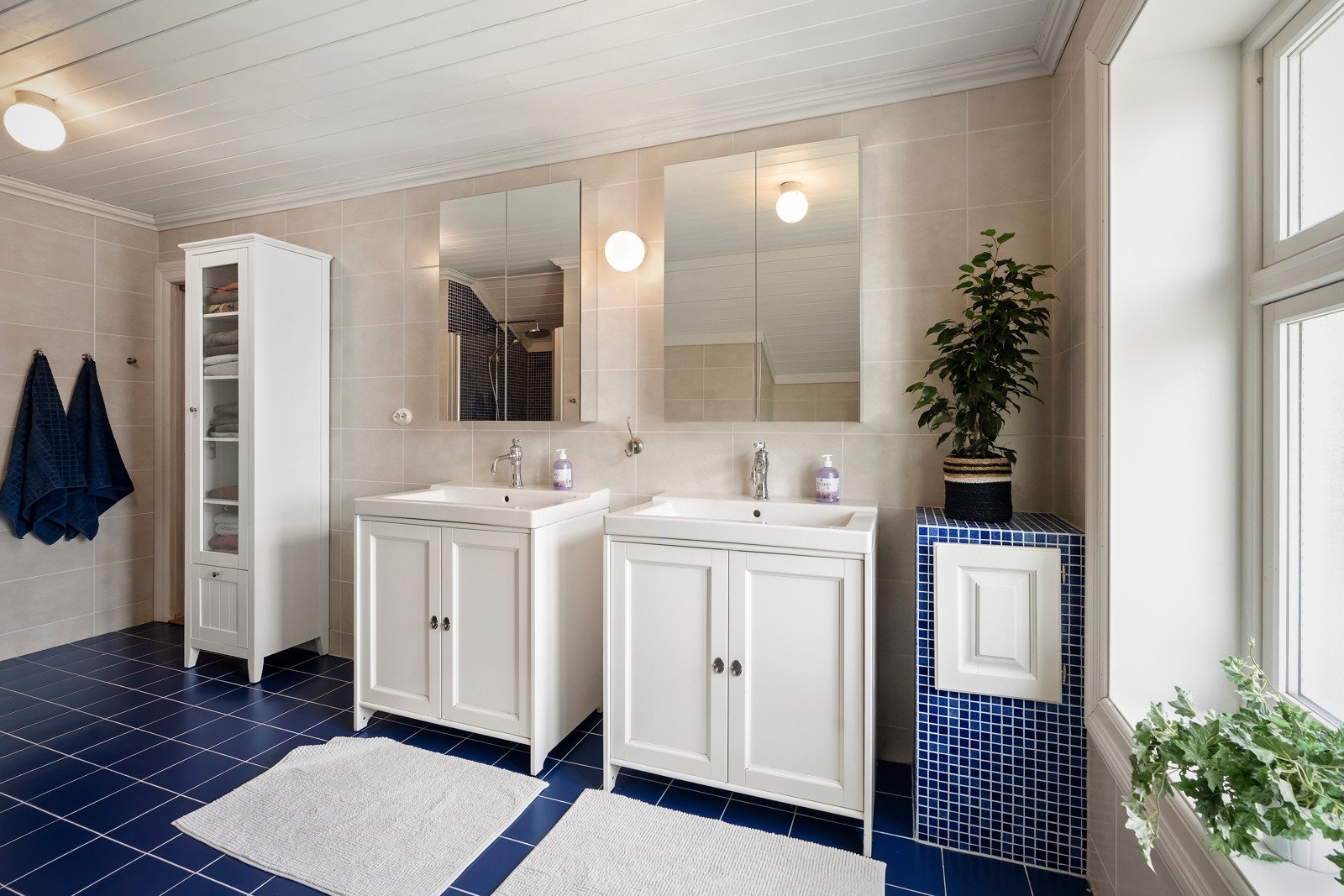 Badet er utstyrt med dusjnisje med glassdør, opplegg for badekar, 2 servanter med skap og porslensvask, 2 speilskap, gulvmontert wc og skittentøysjakt ned til vaskerom. Galleribilde