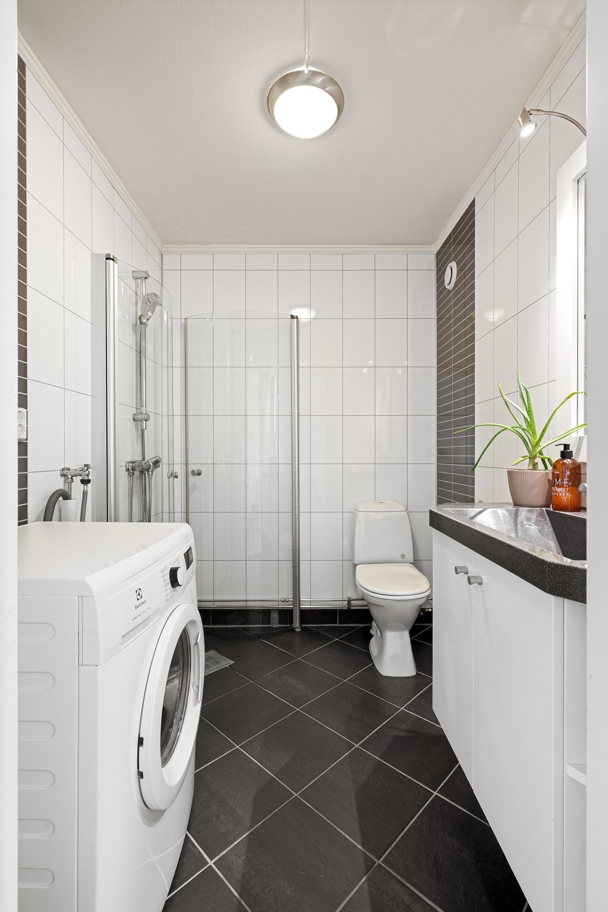 Badet inneholder servantinnredning, toalett, dusjhjørne med innfellbare dører og røropplegg for vaskemaskin Galleribilde