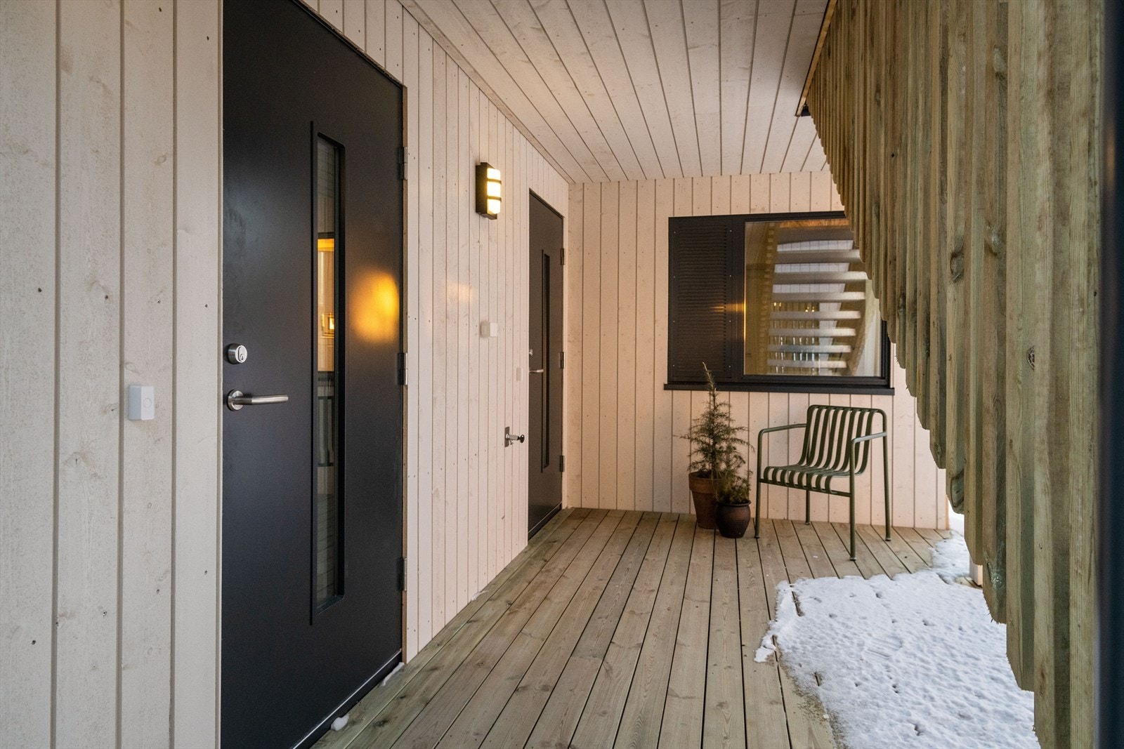 Inngangsparti til leilighet og hybel. Ytterdørene er begge i antrasitt farge, med glassfelt. Terrassedekket gir en hyggelig og ren sone, og det er plass til stol og beplatning utenfor. Galleribilde
