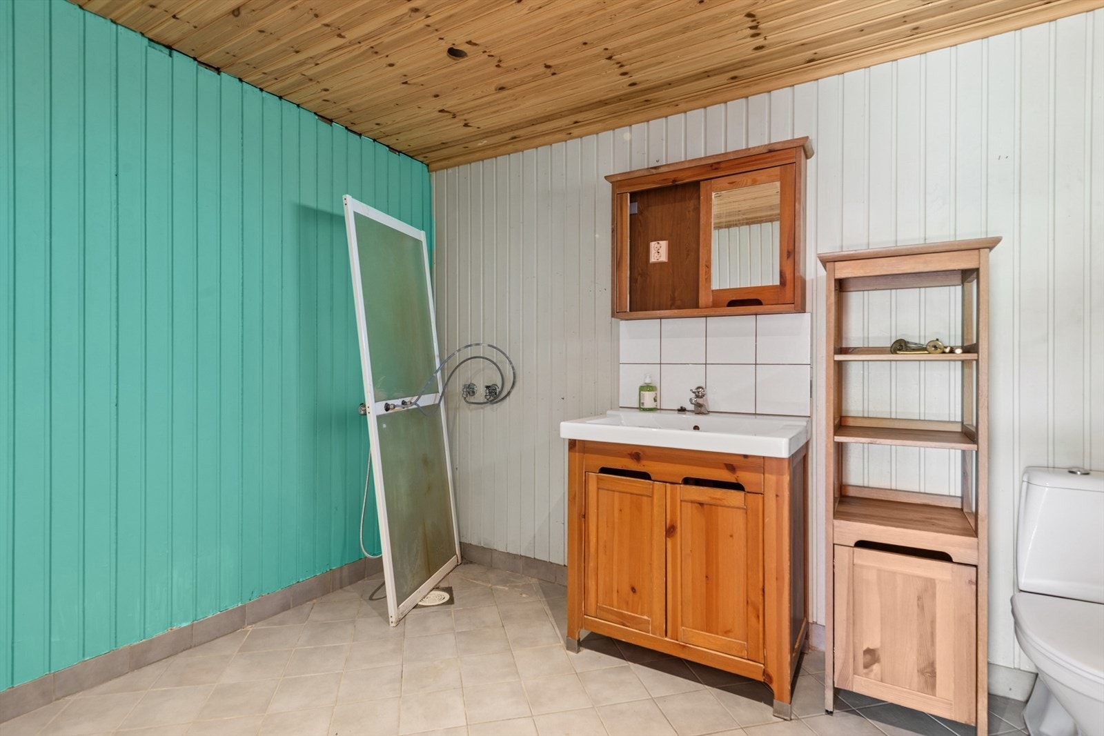 Baderommet er utstyrt med gulvstående klosett og en nedfelt servant, samt kun bakveggen på et dusjkabinett. Galleribilde