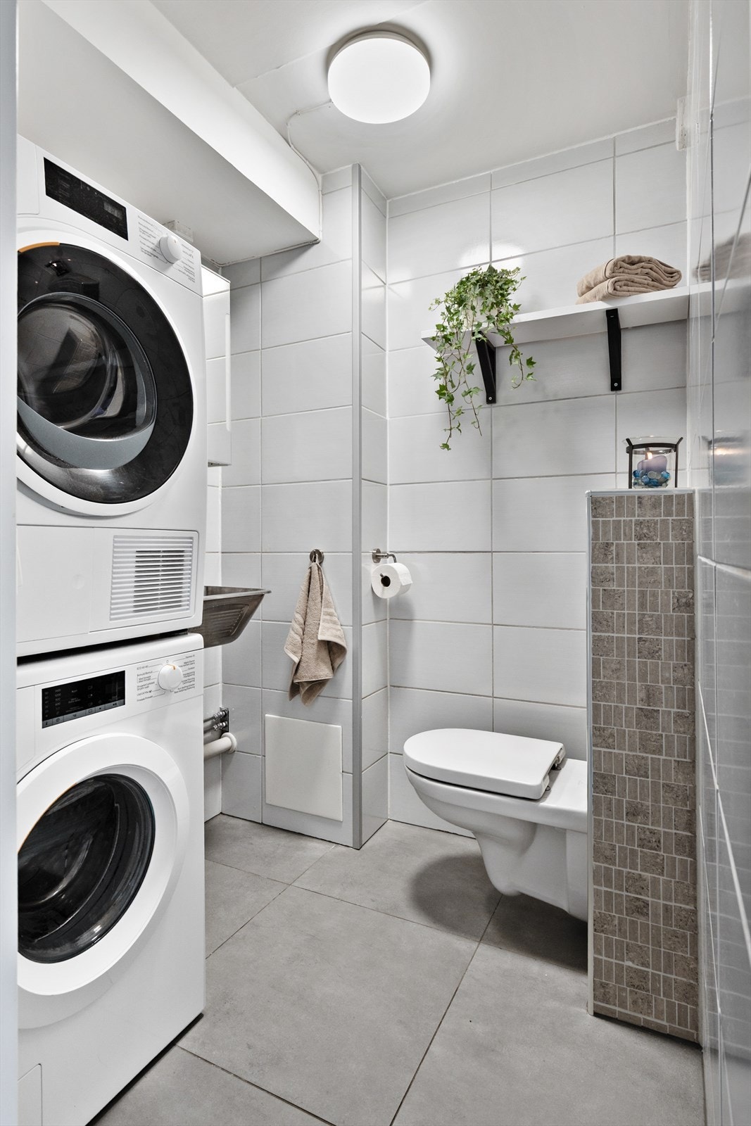 Her er det flislagt på gulv og vegger, innredet med vegghengt klosett og vaskekum. Det er både plass og opplegg for vaskemaskin og tørketrommel. Galleribilde