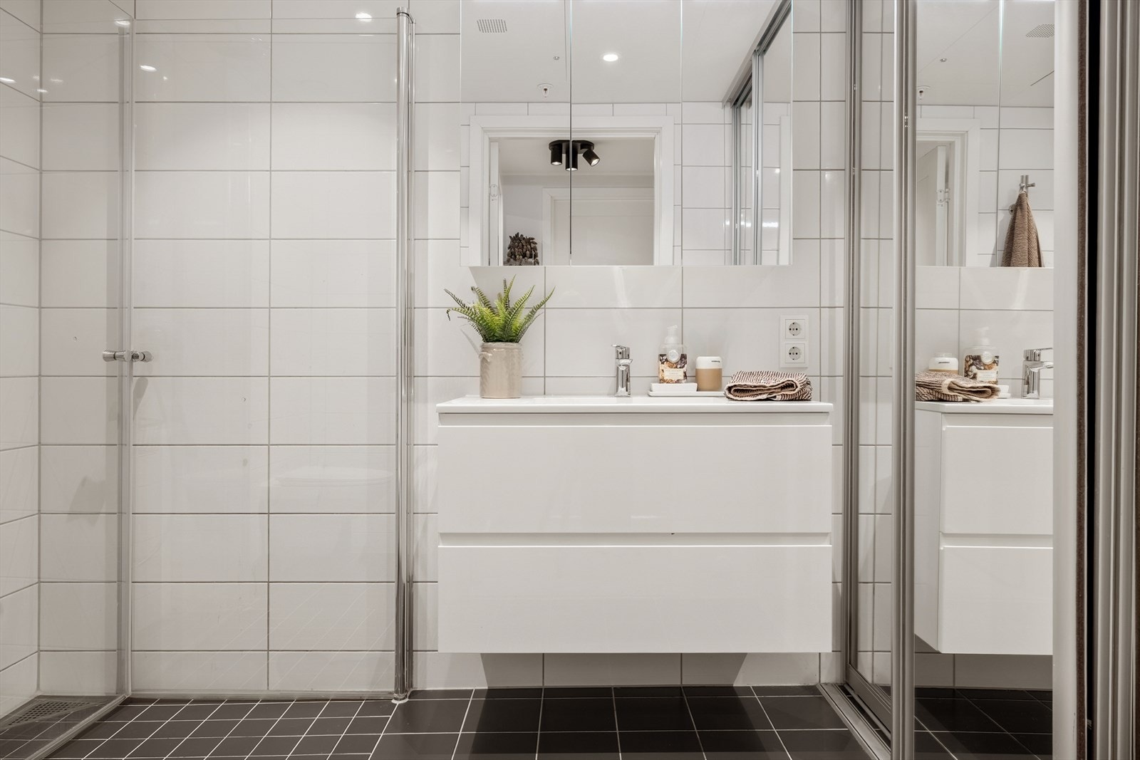 Badet har moderne løsninger med vegghengt toalett, helstøpt servant, skuffer under servant med slette fronter, dusjdører i klart glass og opplegg for vaskemaskin. Galleribilde