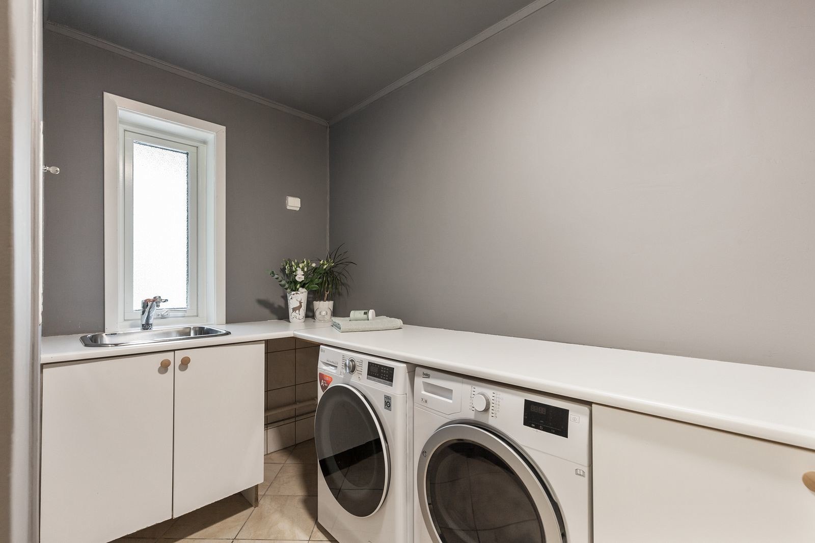 Vaskerom som er praktisk innredet med benkeplater i laminat, underskap, utslagsvask, opplegg for vaskemaskin og tørketrommel samt varmtvannstank. Galleribilde