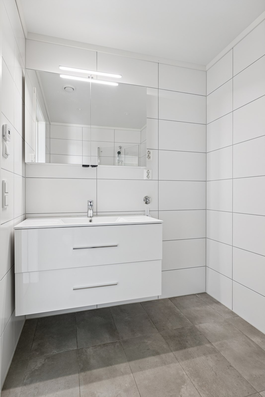 Badet har dusjhjørne med innfellbare glassdører, vegghengt toalett og moderne baderomsinnredning, samt opplegg for vaskemaskin. Galleribilde