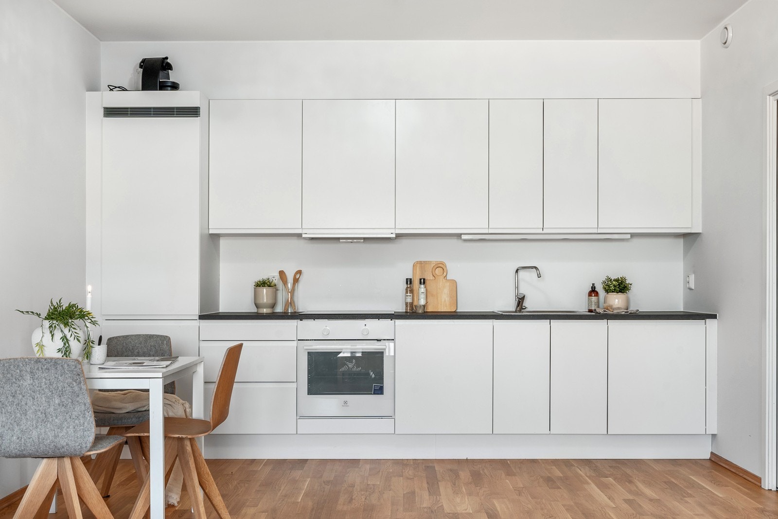 Kjøkkeninnredningen har det man trenger funksjonelt plassert på én vegg med hvite, slette fronter og benkeplate i laminat. Galleribilde