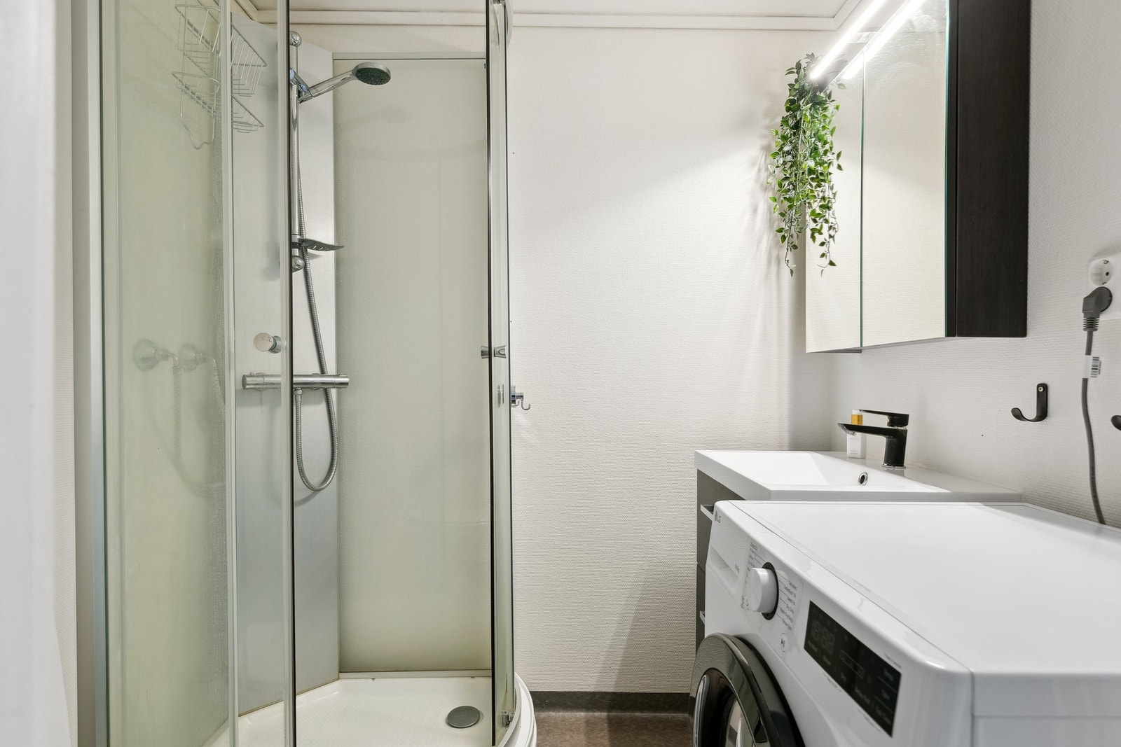 Baderom med dusjkabinett, stilrent servantinnredning med skap og speil, samt opplegg for vaskemaskin. Galleribilde