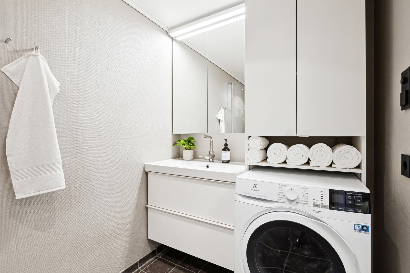 Lyst og fint bad, stilrent servantinnredning med speil, rom for oppbevaring og opplegg for vaskemaskin. Galleribilde