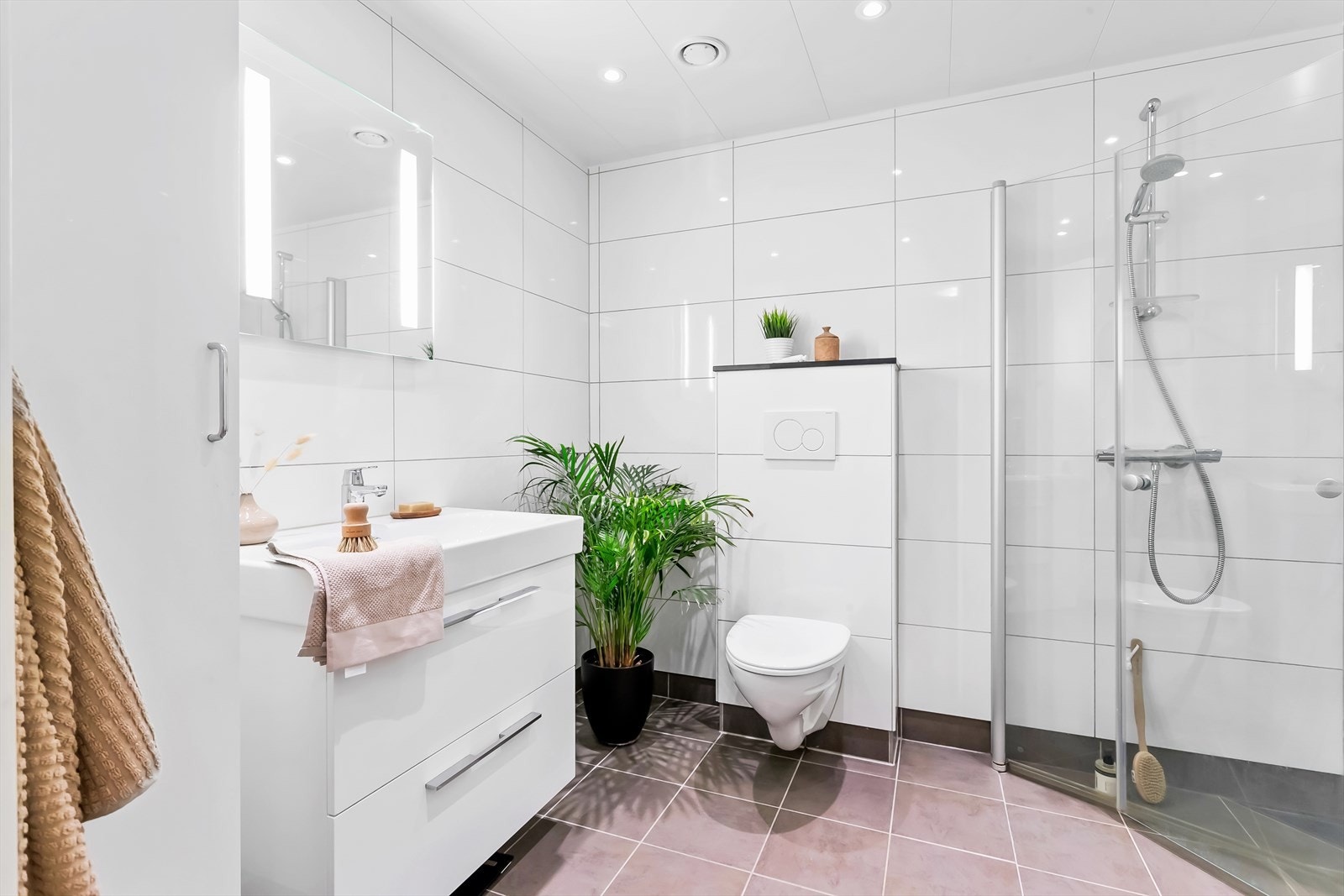 Badet er utstyrt med moderne servant i baderomsmøblement med oppbevaring, speil med integrert belysning over servant, høyskap, vegghengt toalett og dusjhjørne med innfellbare dører i glass. Galleribilde