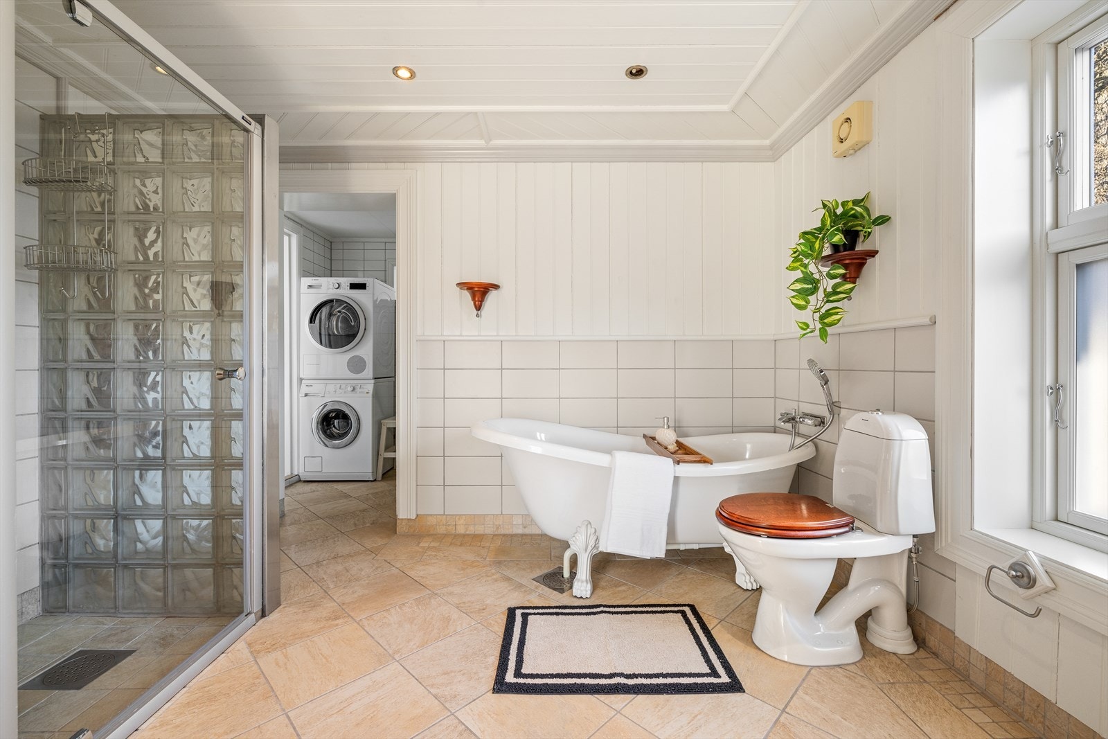 Badet er utstyrt med både frittstående badekar og dusjhjørne. Gulvmontert toalett og servantinnredning med speilskap og sideskap. Galleribilde