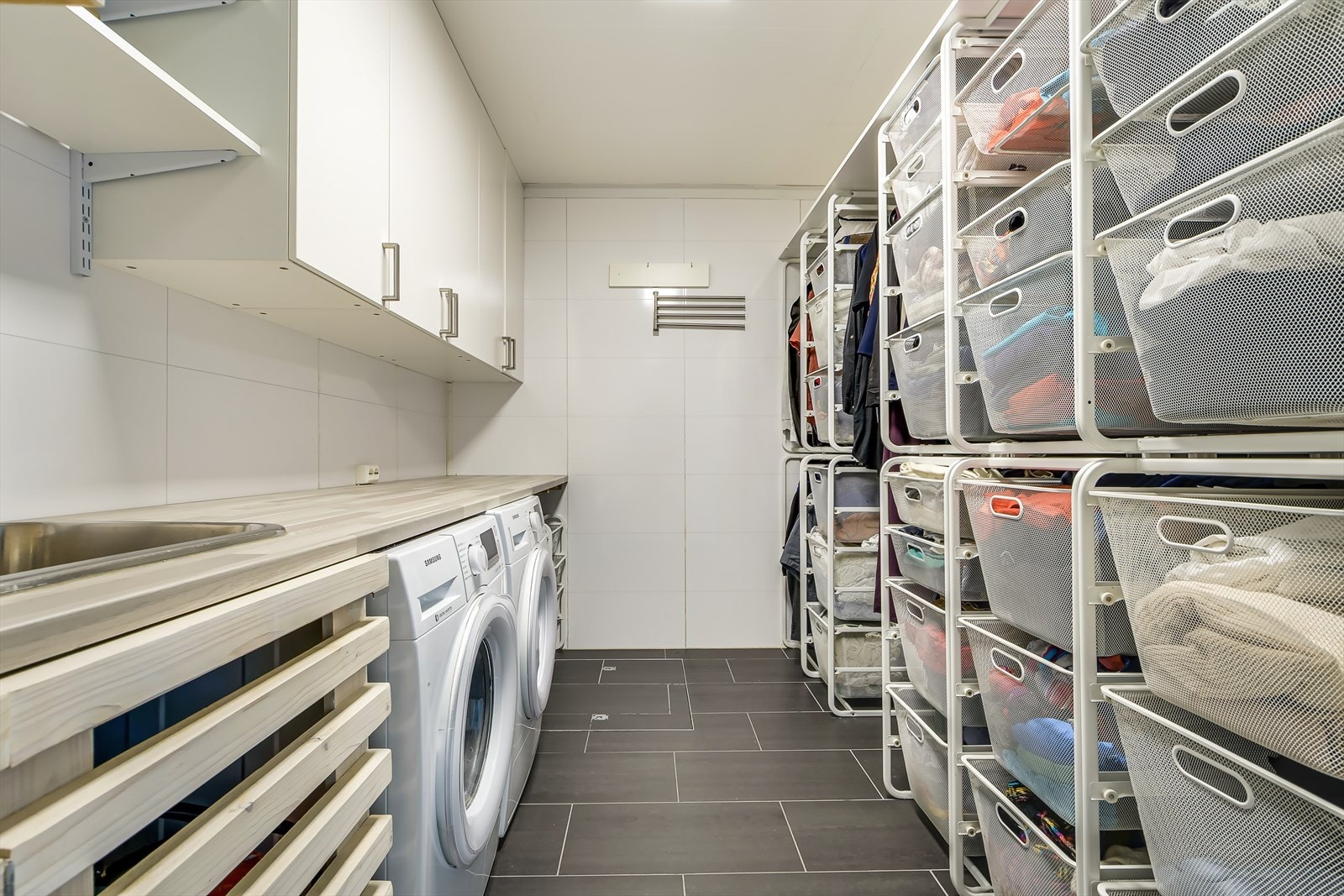 Stort bod som er innredet som vaskerom med vask og opplegg for vaskemaskin og tørketrommel. Galleribilde