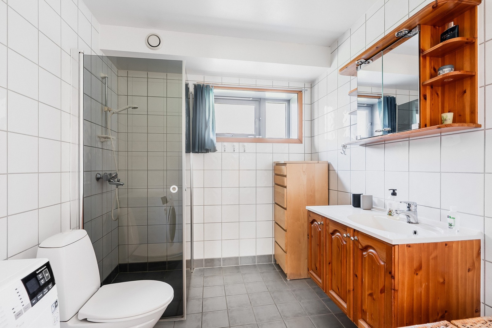 Flislagt bad med varmekabler i gulvet. Dusjhjørne med glassvegger, heldekkende servant og plass til vaskemaskin. Galleribilde