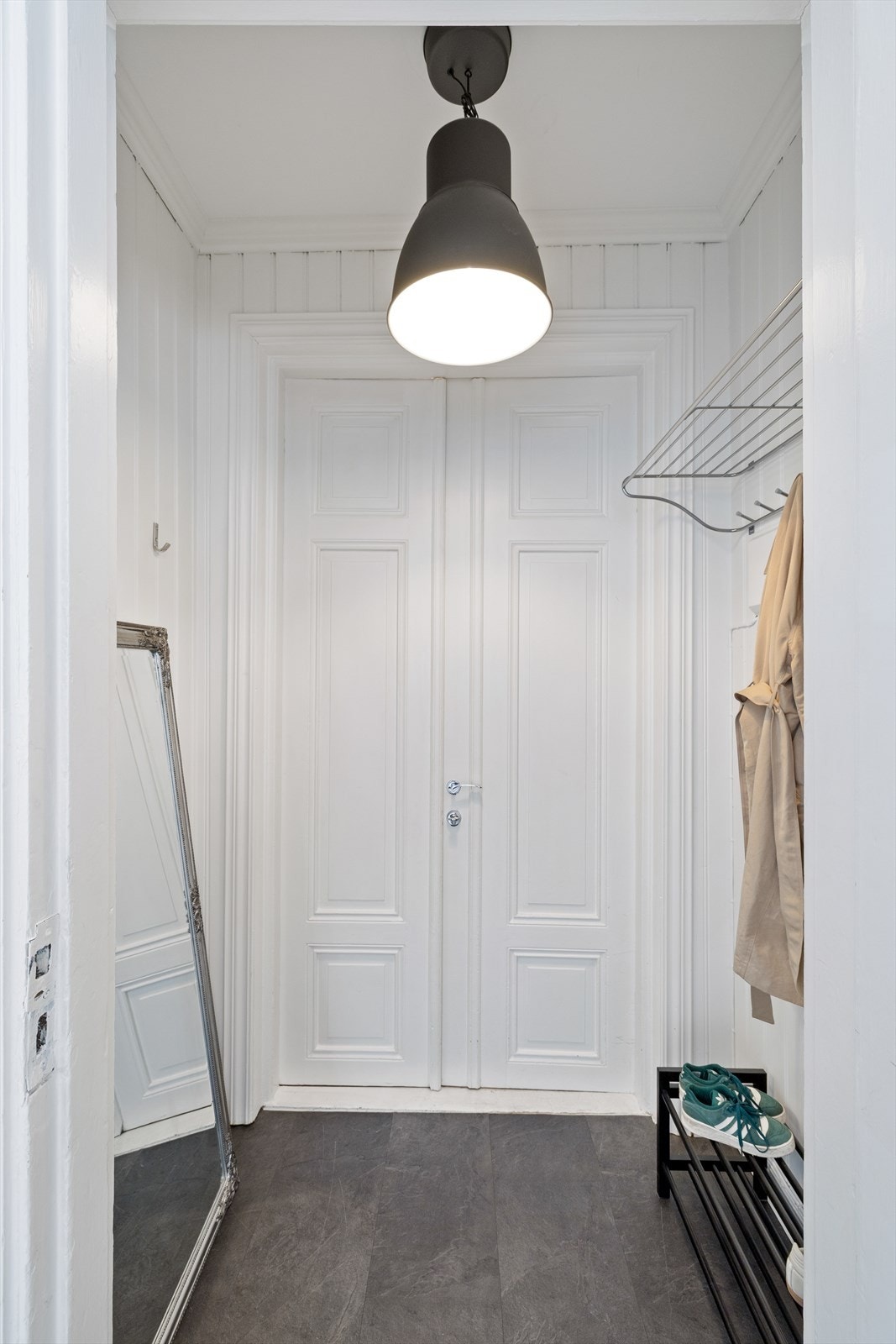 Via en nydelig inngangsdør kommer man inn i leilighetens entre. Her er det plass til oppbevaring av ytterklær på vegghengt knaggrekke, og mulighet for å skostativ. Galleribilde