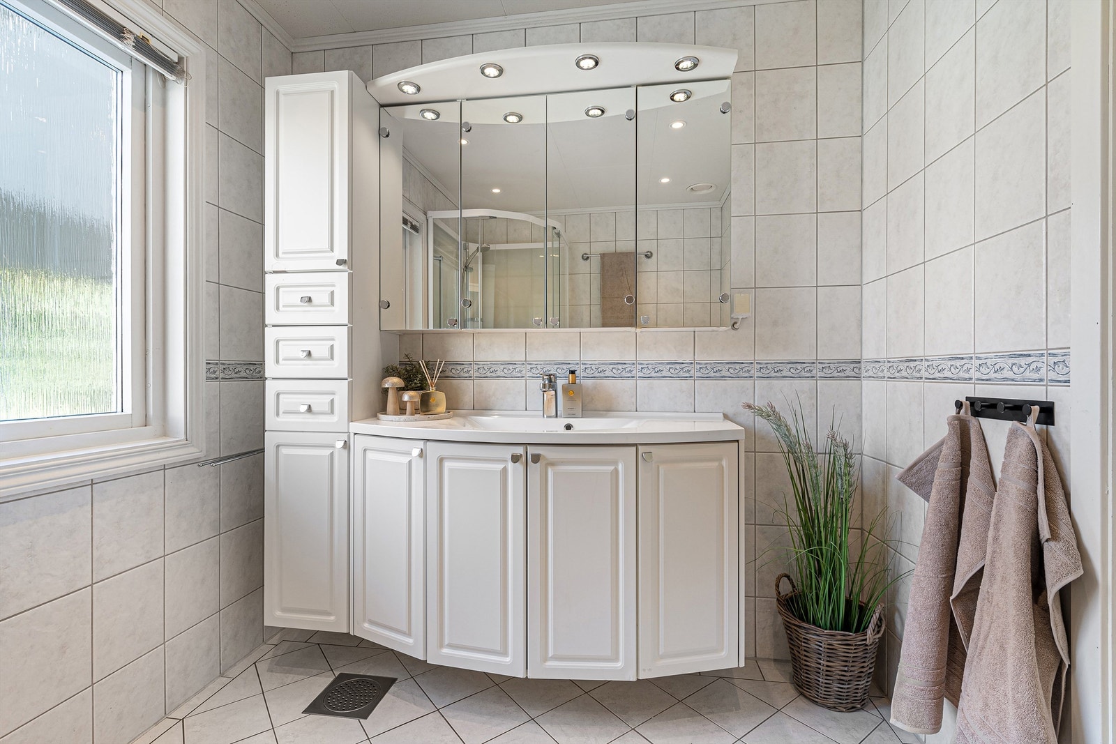 Stor og innholdsrik baderomsinnredning med profilerte fronter og ovenpåliggende servant med ett-greps armatur. Speilskap med overlys over servant. Galleribilde