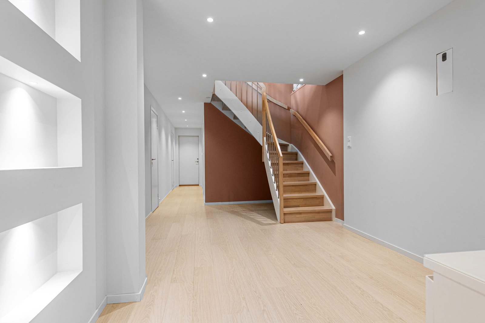 Gang/trapperom i underetasjen. Hvite glatte innerdører. Innfelte nisjer med lys i vegg. Det er montert varmepumpe i gangen. Galleribilde