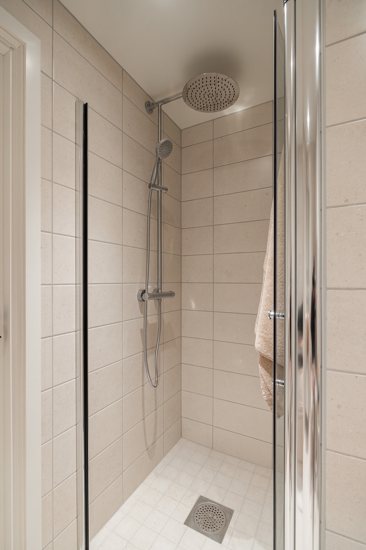 I hjørnet er det en dusjløsning med innfellbare glassdører, utstyrt med både regnfallsdusj og håndholdt dusjfunksjon. Galleribilde