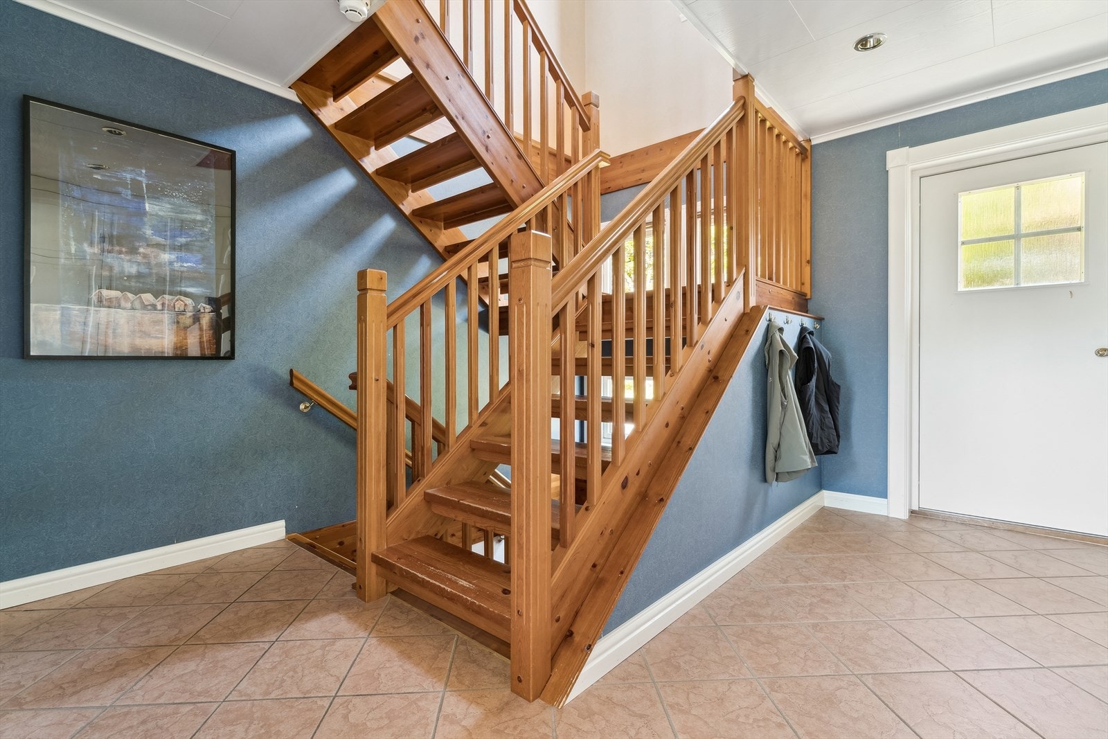 Velkommen inn. Her frå inngang til 1.etasje, ein romsleg entré med flis på golv. Det er også inngang i underetasjen, både direkte frå garasje og mot sør. Galleribilde