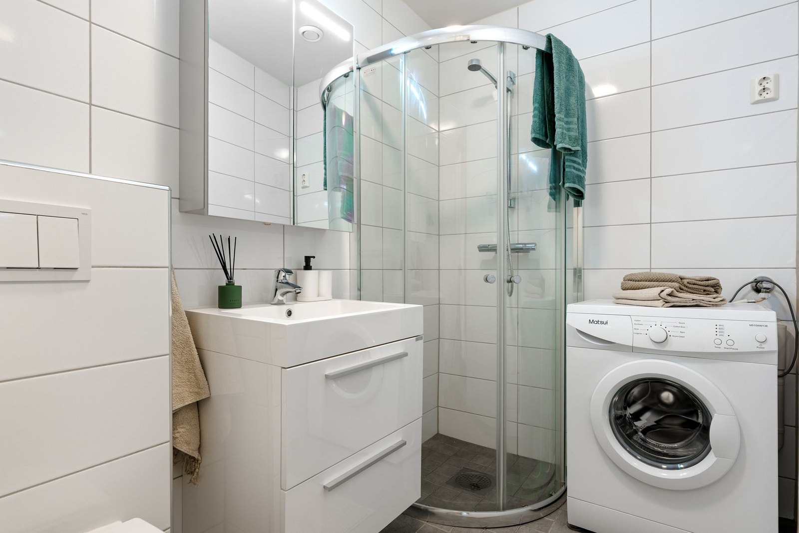 Lyst flislagt baderom utstyrt med varme i gulv, servantskap, dusj, toalett og opplegg for vaskemaskin. Galleribilde