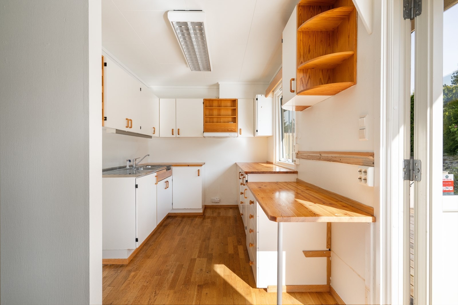 Det er benkebeslått oppvaskkum i rustfritt stål og plass for frittstående komfyr. Over kokesone er det kjøkkenventilator med avtrekk ut. Galleribilde