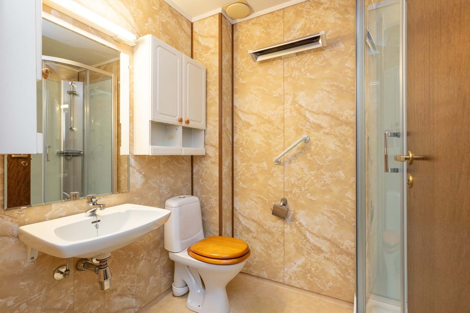 I hovedetasjen er det et eldre baderom med vinylbelegg på gulv, baderomsplater på vegger og tak-ess plater i himling. Rommet er utstyrt med vegghengt servant med speilflate og belysning over vask samt vegghengte skaper på siden. Galleribilde