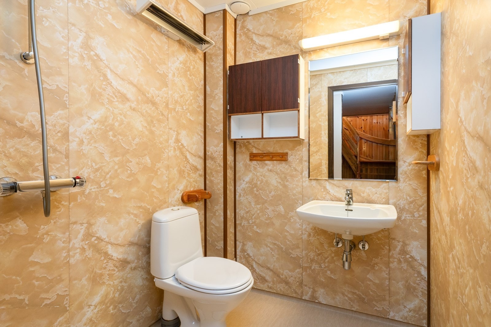 Underetasjen har også et eldre baderom hvor det er vinylbelegg på gulv, baderomspanel på vegger og tak-ess plater i himling. Innredning med servant på vegg, speil og lys over servant samt vegghengte skaper. Åpen dusjnisje med armatur. Galleribilde