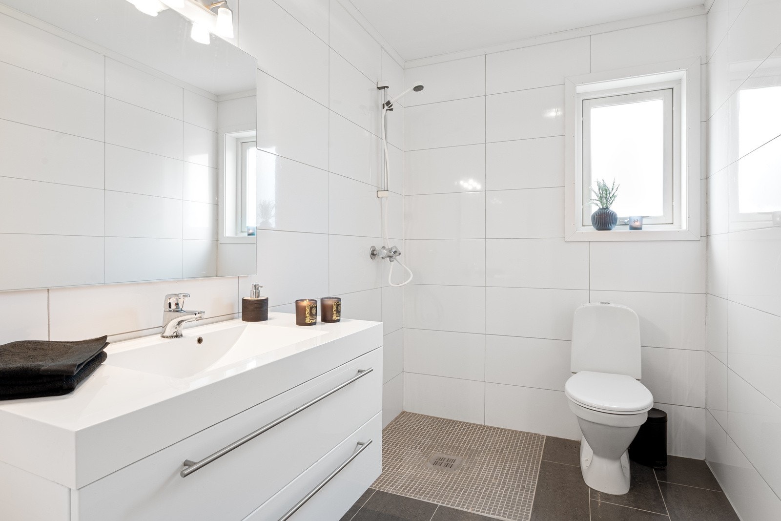 Tiltalende og lyst bad 1. etasje med dusjhjørne, WC og hvit innredning med servant og speil. Galleribilde