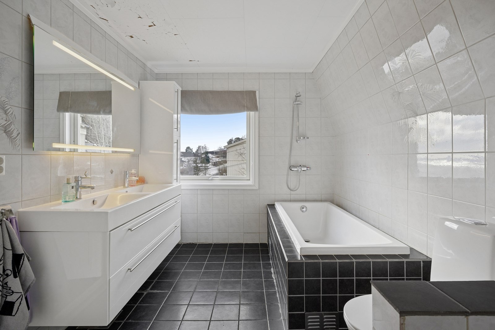 Helfliset bad med varme i gulv. Rommet fremstår som en romslig velværeavdeling som byr på baderomsinnredning bestående av benkeskap og veggskap med glatte fronter i høyglanset utførelse, to servanter. Galleribilde