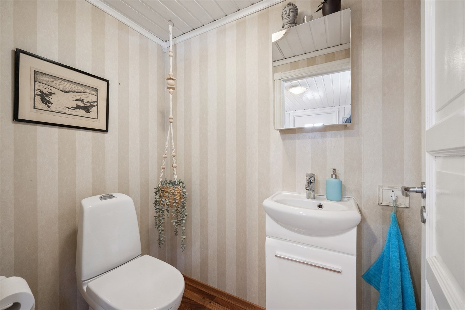 Toalettrom, innredning med benkeskap med glatte fronter. Veggskap med speilfront over servant. Gulvstående klosett og servant. Laminat på gulv. Tapet på vegger. Galleribilde