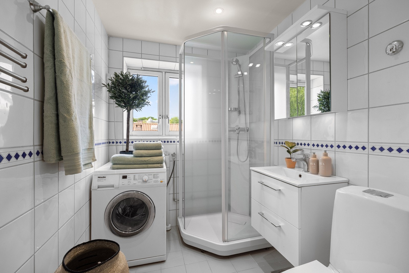 Pent flislagt bad utstyrt med gulvstående toalett, servantinnredning med servant, ettgreps blandebatteri, dusjkabinett, plass og opplegg for vaskemaskin. Galleribilde