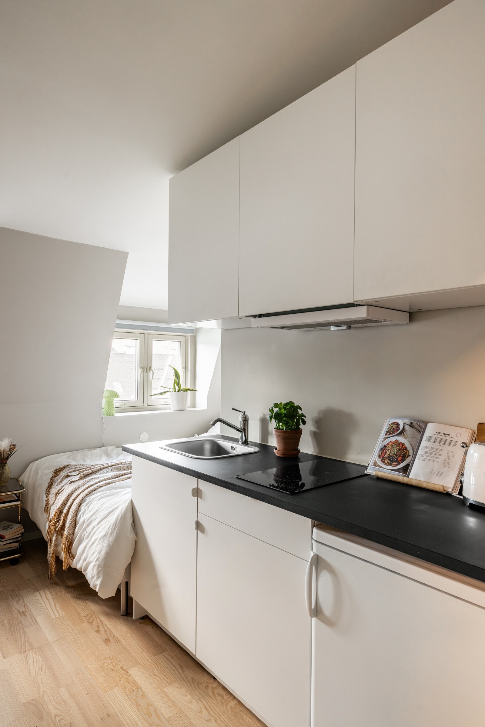 Lys kjøkkeninnredning fra 2019/20 med benkeplate av laminat, nedfelt oppvaskkum med ett-greps kjøkkenarmatur, platetopp nedfelt i benkeplate og kjøleskap i benk. Det er ventilator i overskap med komfyrvakt. Galleribilde