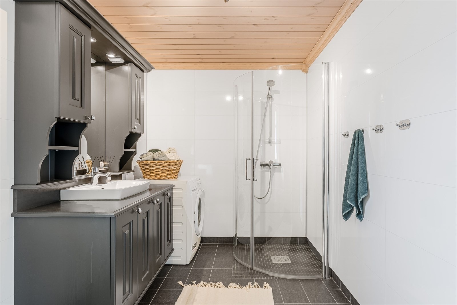 Fra entréen er det dør inn til badet, som har flislagt gulv og baderomsplater på vegger. Badet er innredet med dusjhjørne, frittstående toalett, opplegg for vaskemaskin, og en solid og pen innredning i heltre som står i stil med øvrig inventar i hytta. Galleribilde