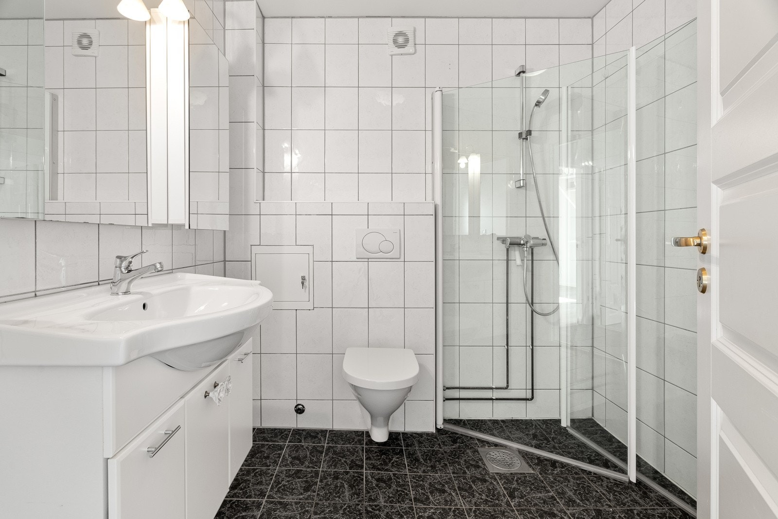 Lyst flisbelagt bad med hjørnedusj med glassdører, toalett og servant. Galleribilde