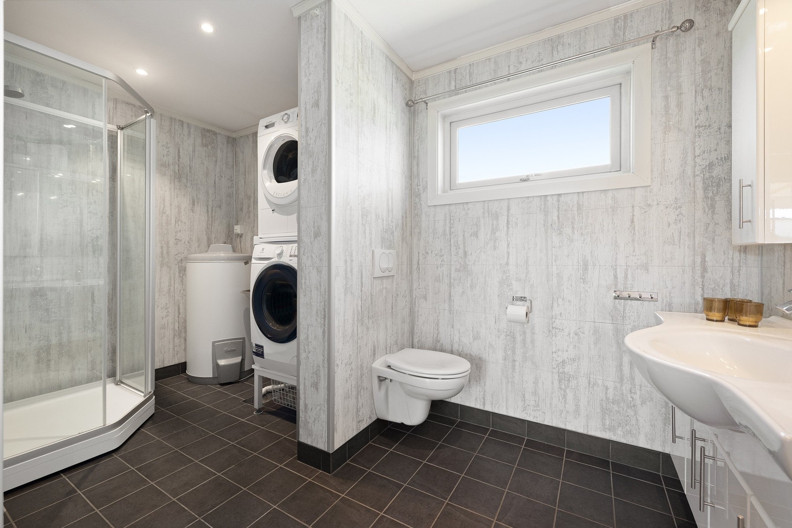 Innredet med vegghengt klosett, heldekkende servant, speil, overskap med lys, dusjkabinett og utslagsvask Galleribilde