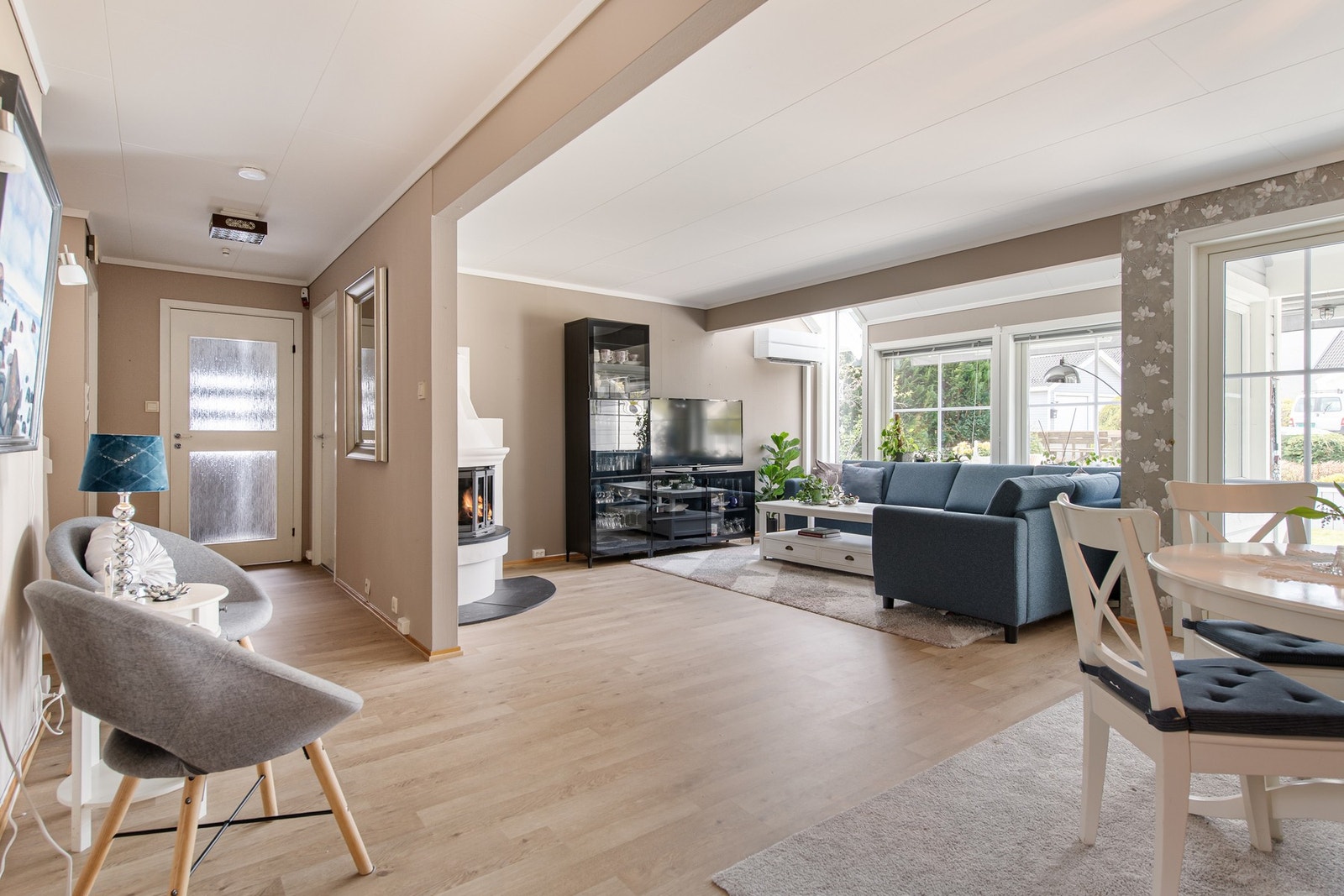 Her har du en lys og åpen stue med store vindusflater ut mot hagen og peis som kan nytes fra både spiseplass og sofa Galleribilde