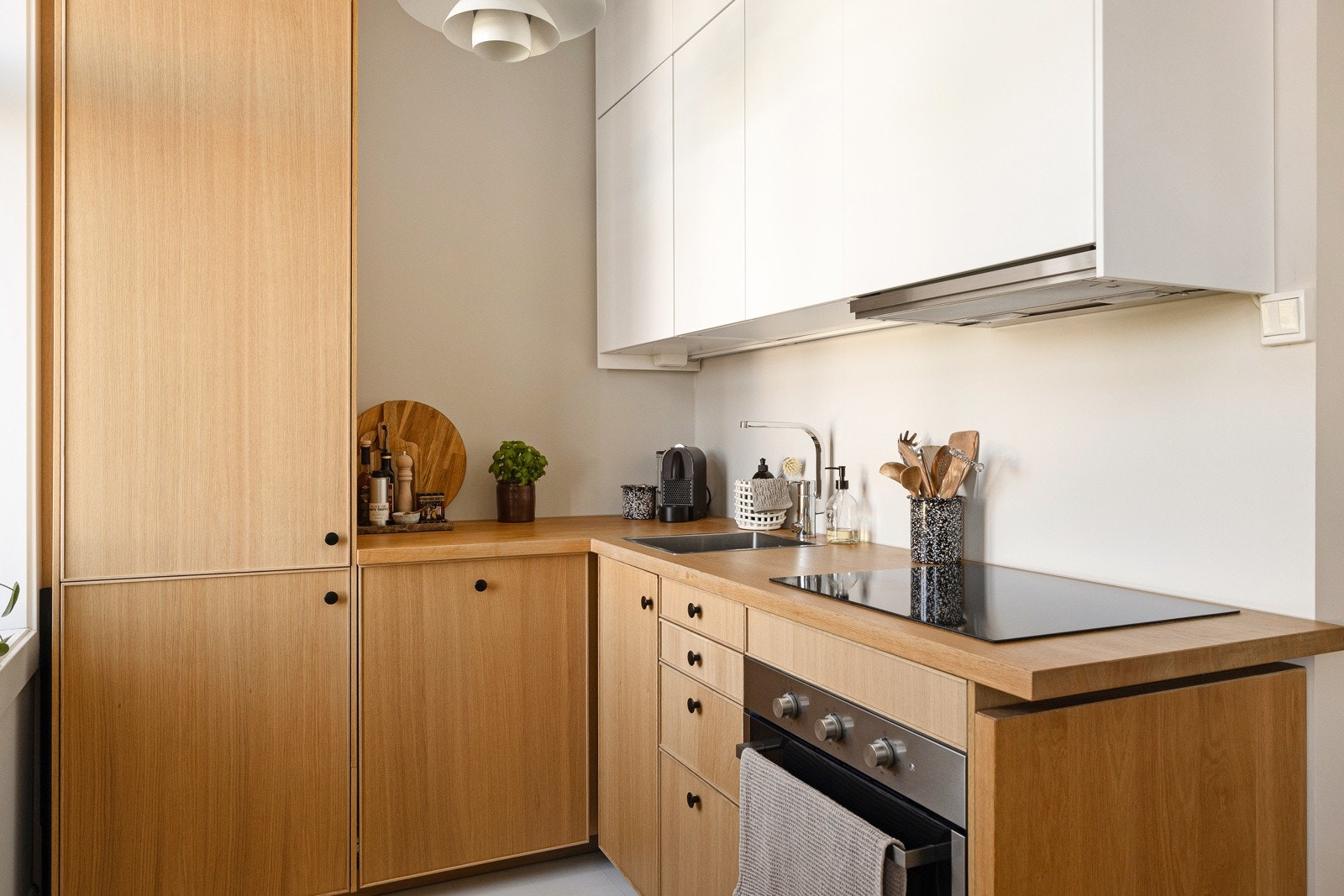 Stilren kjøkkeninnredning med eikefinérte fronter på benkeskap og høyskap, overskap med slette fronter og benkebelysning Galleribilde